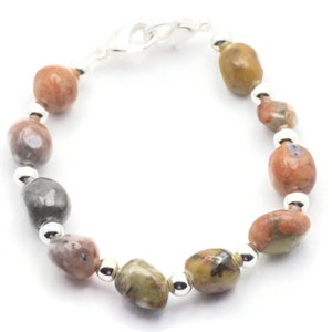 May include: A bracelet made with brown, gray, and white stones. The bracelet has a silver clasp.