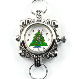 May include: A silver pocket watch with a white face and a Christmas tree design. The watch has a silver chain and a silver clasp.