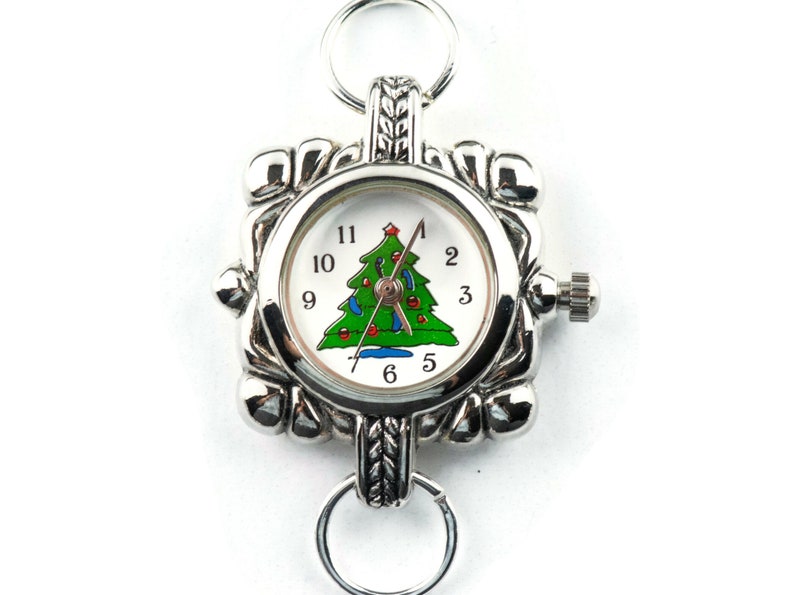 May include: A silver pocket watch with a white face and a Christmas tree design. The watch has a silver chain and a silver clasp.