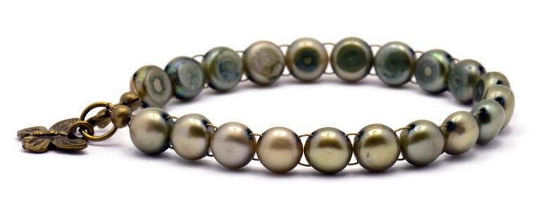 Op de afbeelding: Een armband gemaakt van groene parels met een bronzen vlinderbedel.
