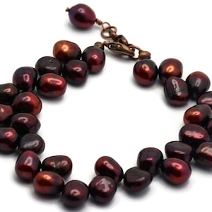 May include: A dark red freshwater pearl bracelet with a copper clasp. The pearls are irregular in shape and have a slight sheen.
