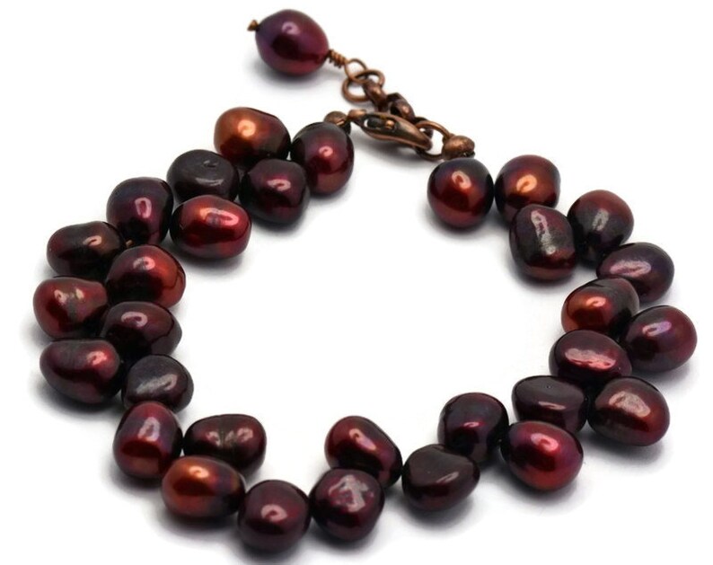 May include: A dark red freshwater pearl bracelet with a copper clasp. The pearls are irregular in shape and have a slight sheen.