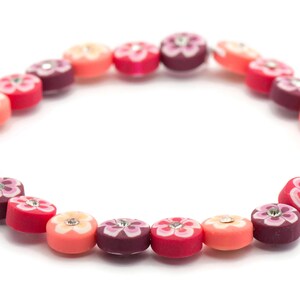 K&ouml;nnte beinhalten: Ein farbenfrohes Armband aus runden Perlen mit Blumenmustern und Strasssteinen. Die Perlen sind in den Farben Rosa, Rot und Lila.