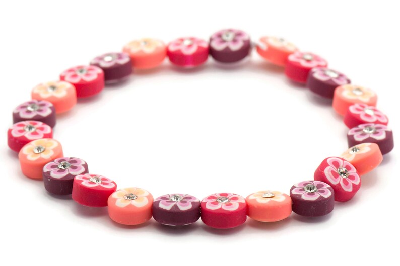 K&ouml;nnte beinhalten: Ein farbenfrohes Armband aus runden Perlen mit Blumenmustern und Strasssteinen. Die Perlen sind in den Farben Rosa, Rot und Lila.