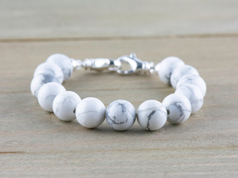 Peut inclure: Un bracelet en perles d'howlite blanches avec un fermoir argent&eacute;. Les perles sont rondes et ont un motif marbr&eacute;.
