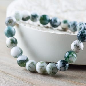 May include: A green and white agate beaded bracelet. The beads are round and have a natural, marbled pattern.