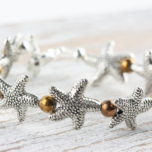 May include: Silver bracelet with a series of starfish charms and gold-toned beads.