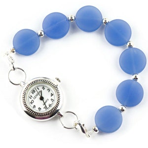 Peut inclure: Une montre argent&eacute;e avec un cadran blanc et des chiffres noirs est attach&eacute;e &agrave; un bracelet compos&eacute; de perles bleu clair.