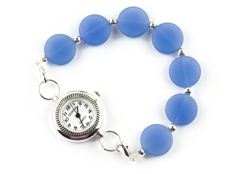 Peut inclure: Une montre argent&eacute;e avec un cadran blanc et des chiffres noirs est attach&eacute;e &agrave; un bracelet compos&eacute; de perles bleu clair.