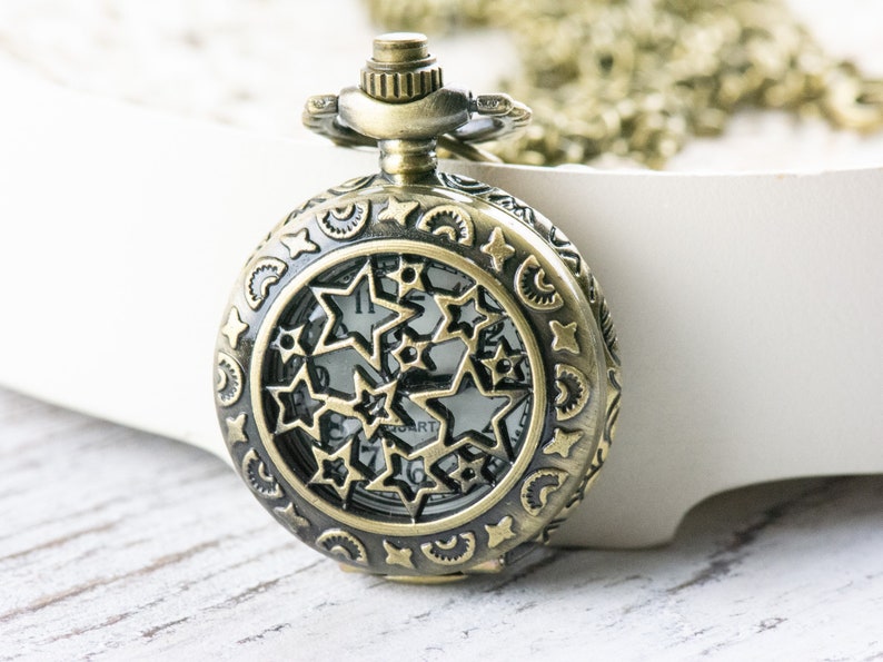 May include: A gold-toned pocket watch with a star-shaped design on the face. The watch has a chain attached to it.