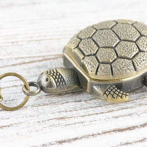 May include: A bronze turtle pendant with a chain. The turtle has a detailed shell and a textured surface.