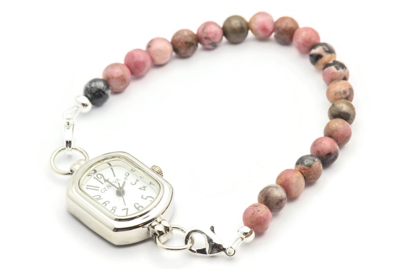 K&ouml;nnte beinhalten: Eine silberne Uhr mit quadratischem Zifferblatt und schwarzen r&ouml;mischen Ziffern an einem rosafarbenen und braunen Perlenarmband.