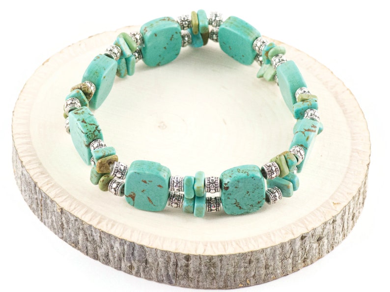 Op de afbeelding: Turquoise en zilveren armband met vierkante turquoise kralen en zilveren tussenkralen. De armband ligt op een houten oppervlak.