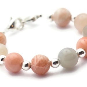 May include: A bracelet made of light pink, gray, and white sunstone beads with silver accents.
