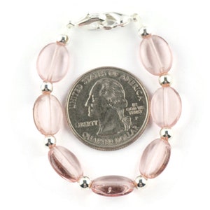 May include: A pink glass bead bracelet with a silver clasp. The bracelet is about the size of a US quarter.