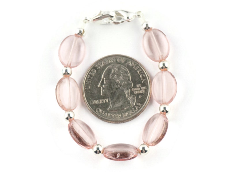 May include: A pink glass bead bracelet with a silver clasp. The bracelet is about the size of a US quarter.