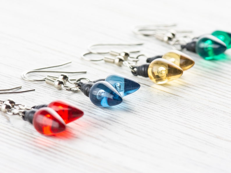 Op de afbeelding: Een set van vijf paar hangende oorbellen met lichtbollen van glas in de kleuren rood, blauw, geel, groen en helder. De oorbellen zijn gemaakt met zilverkleurige metalen haakjes.