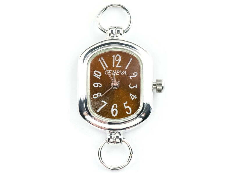 May include: Silver Geneva watch with a rectangular face and a brown dial. The watch has white numerals and hands, and two silver rings for attachment. A classic accessory.