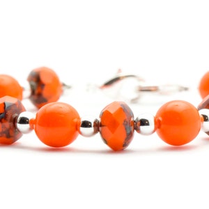 May include: Orange and black glass bead bracelet with silver accents. The bracelet has a clasp closure.