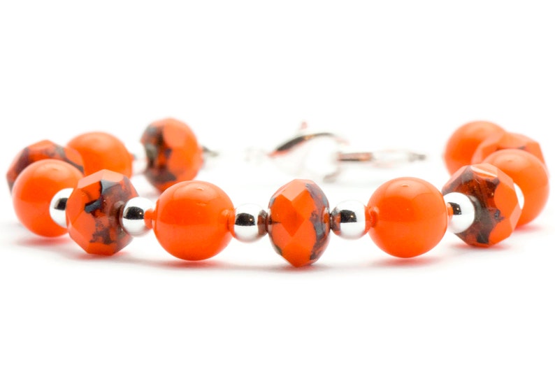 May include: Orange and black glass bead bracelet with silver accents. The bracelet has a clasp closure.