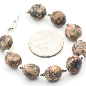 May include: A bracelet made with brown, black, and pink speckled oval-shaped beads separated by silver spacers. The bracelet is shown next to a US quarter for size comparison.