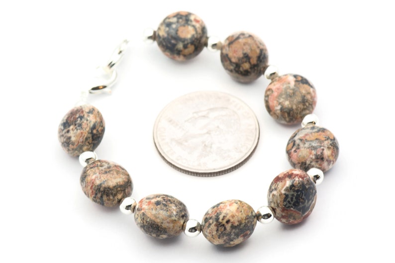 May include: A bracelet made with brown, black, and pink speckled oval-shaped beads separated by silver spacers. The bracelet is shown next to a US quarter for size comparison.