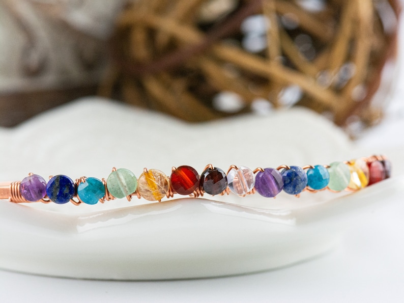 K&ouml;nnte beinhalten: Ein Regenbogen-Chakra-Armband aus Kupferdraht und verschiedenen Edelsteinen, darunter Amethyst, Lapislazuli, T&uuml;rkis, Aventurin, Citrin, Karneol, Granat, klarer Quarz und Amethyst.