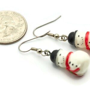 May include: A pair of silver snowman earrings with red and black accents. The earrings are about the size of a US quarter.