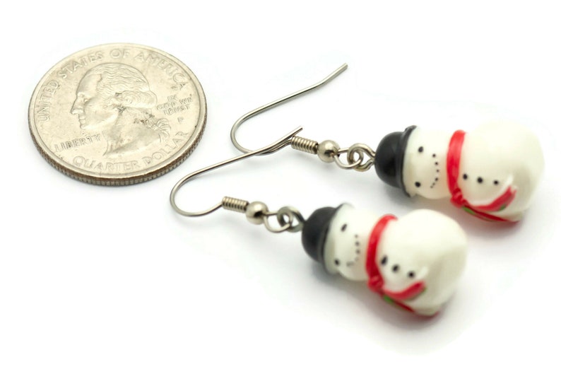 May include: A pair of silver snowman earrings with red and black accents. The earrings are about the size of a US quarter.