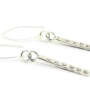 May include: A pair of silver dangle earrings with a textured bar and a circle hook.