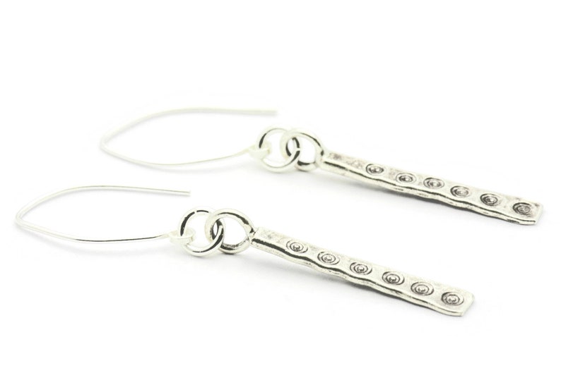 May include: A pair of silver dangle earrings with a textured bar and a circle hook.