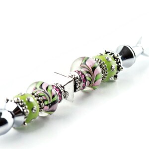 Peut inclure: Un couteau &agrave; beurre en argent avec un manche d&eacute;coratif en perles de verre vertes et roses avec des accents argent&eacute;s. Le manche est orn&eacute; de petits strass roses.