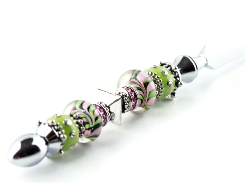 Peut inclure: Un couteau &agrave; beurre en argent avec un manche d&eacute;coratif en perles de verre vertes et roses avec des accents argent&eacute;s. Le manche est orn&eacute; de petits strass roses.