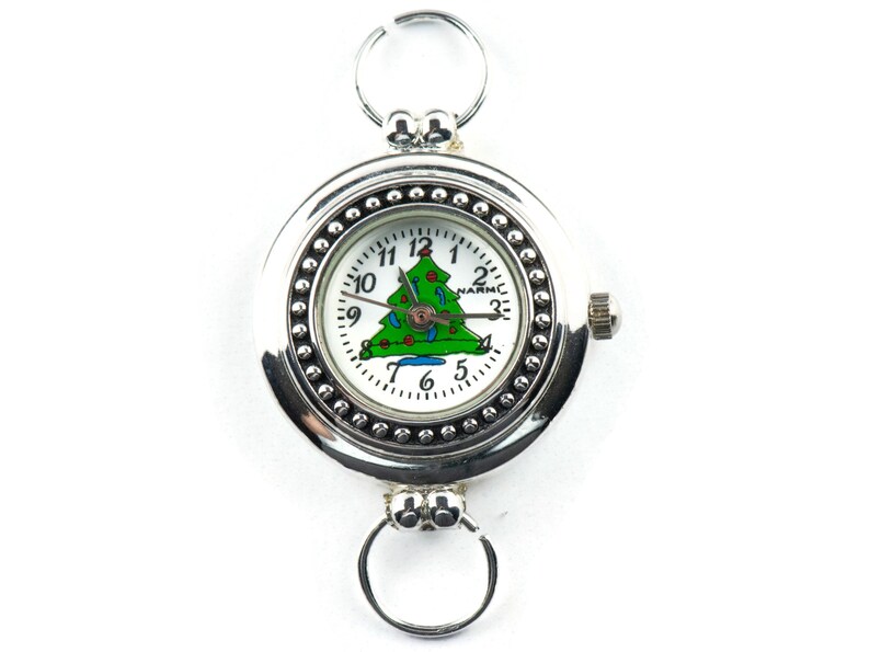 May include: A silver pocket watch with a white face and a green Christmas tree design. The watch has a silver chain and a small knob on the side.