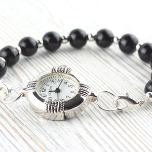 Pu&ograve; includere: Bracciale orologio Geneva con quadrante argentato, quadrante bianco e numeri neri. Il bracciale &egrave; composto da grandi perle nere lucide e dettagli argentati. Con chiusura.
