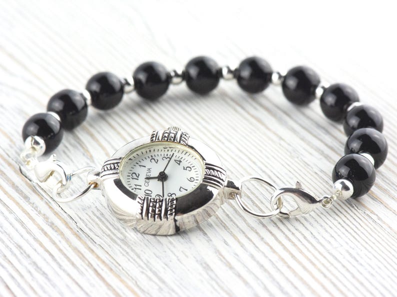 Pu&ograve; includere: Bracciale orologio Geneva con quadrante argentato, quadrante bianco e numeri neri. Il bracciale &egrave; composto da grandi perle nere lucide e dettagli argentati. Con chiusura.