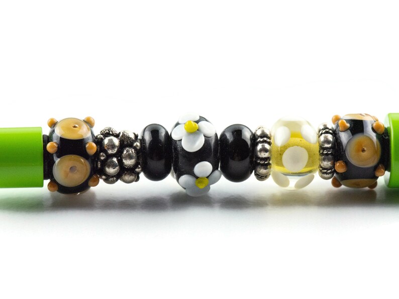 May include: A close-up of a bracelet with black, white, and yellow beads. The beads are arranged in a pattern and have a variety of shapes and sizes. The bracelet is made of glass and metal.