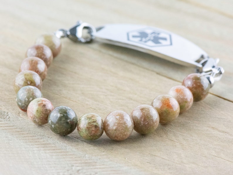 Pu&ograve; includere: Un braccialetto di perline rotonde multicolori nei toni del verde, marrone e arancione. Include una targhetta identificativa medica color argento con un simbolo medico e una chiusura.
