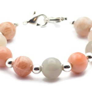 May include: A bracelet made with alternating light gray, peach, and pink moonstone beads with silver spacers.