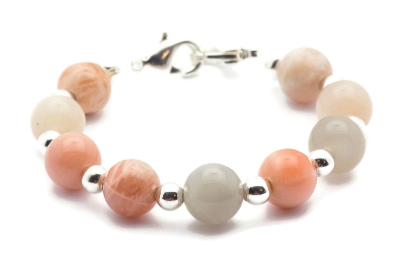 May include: A bracelet made with alternating light gray, peach, and pink moonstone beads with silver spacers.