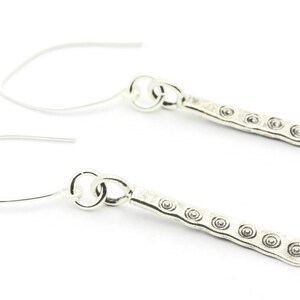 May include: A pair of silver dangle earrings with a textured bar design and small circular accents.