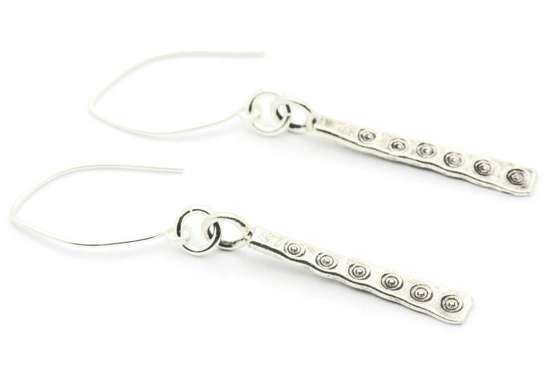 May include: A pair of silver dangle earrings with a textured bar design and small circular accents.