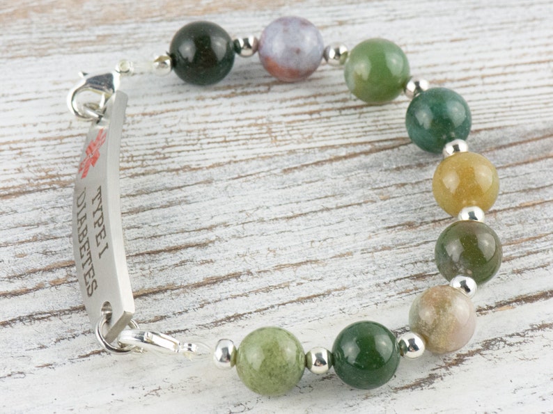 K&ouml;nnte beinhalten: Ein silbernes Armband mit einem medizinischen Anh&auml;nger, auf dem "Typ 1 Diabetes" steht. Das Armband besteht aus gr&uuml;nen, braunen und gelben Achatperlen.