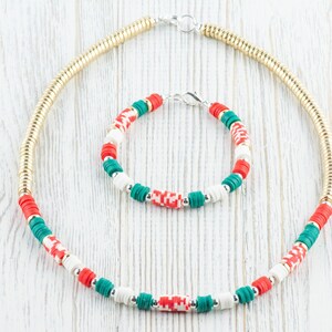May include: A gold chain necklace and a bracelet with red, white, and green beads. The beads are arranged in a repeating pattern.