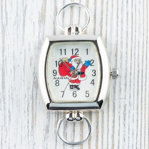 May include: A silver pocket watch with a white face and a Santa Claus design. The watch has a chain attached to it.