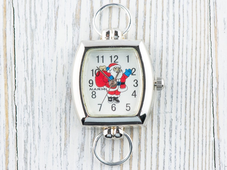 May include: A silver pocket watch with a white face and a Santa Claus design. The watch has a chain attached to it.