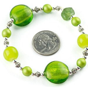 Puede incluir: Un brazalete de cuentas de vidrio verde con cuentas espaciadoras plateadas. El brazalete es aproximadamente del tama&ntilde;o de una moneda de 25 centavos.