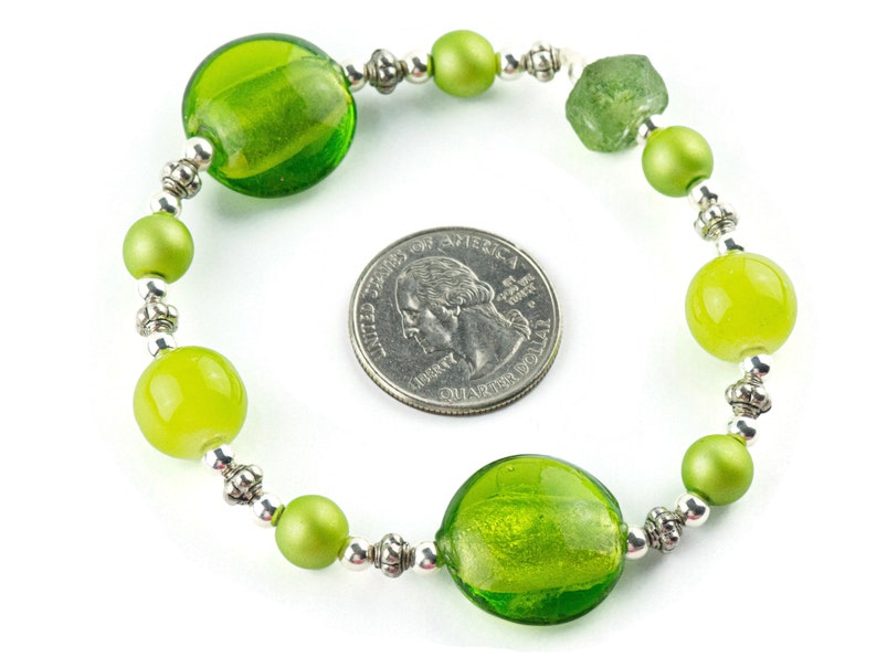 Puede incluir: Un brazalete de cuentas de vidrio verde con cuentas espaciadoras plateadas. El brazalete es aproximadamente del tama&ntilde;o de una moneda de 25 centavos.
