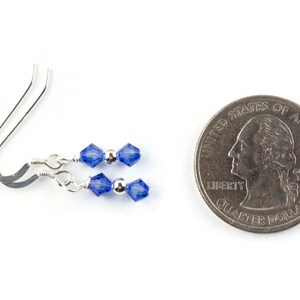 May include: A pair of silver earrings with two blue crystal beads on each earring. The earrings are shown next to a US quarter for size comparison.
