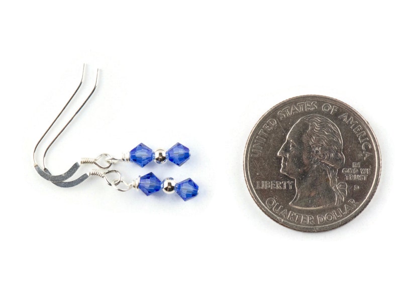 May include: A pair of silver earrings with two blue crystal beads on each earring. The earrings are shown next to a US quarter for size comparison.